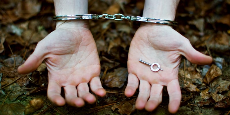 Handcuffed hands open and outstretched holding key